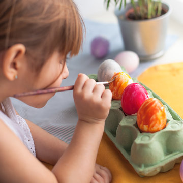 Happy easter! Cute little kid girl painting with blue and red colors Easter eggs. family preparing for Easter. Hands of a girl with a easter egg. close-up. lifestyle