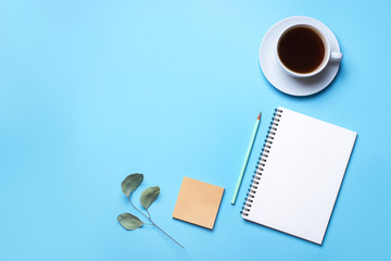 Blue background with notepad, pencil and cup of coffee. Top view with copy space, flat lay.