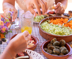 Group of caucasian hands on the wooden table. Mix of vegetables, salad and spinach meatballs. Fresh fruits and drink