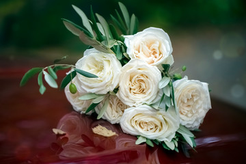 Beautiful wedding bouquet of white roses on a red hood of a car. Close-up. Background, texture. Tinting