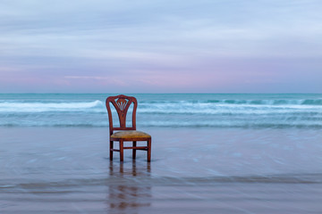 Fototapeta na wymiar Old chair on the ocean coast, dramatic sky, melancholic scene, loneliness, long exposure