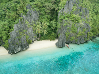 Shipwrecked solo tourist alone on a tiny wooden boat while isolated on shore of a white sand beach paradise getaway on a tropical desert island in the south Pacific ocean