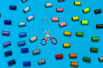 top view creative still life flat lay with reels of multicolored threads and scissors pattern on a blue background