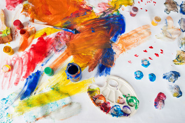 Bright multi-colored childrens drawings with paints, brushes and palette stained with paint