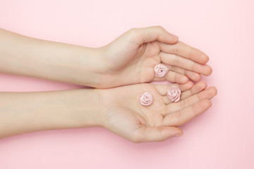Fototapeta premium The woman hands hold rose flowers on a pink background. A thin wrist and natural manicure. Cosmetics for a sensitive skin care. Natural petal cosmetics, anti-wrinkle hand care.