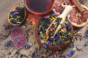 blended tea. black tea with dry flower petals and citrus fruits. dry black tea leaves in a wooden...