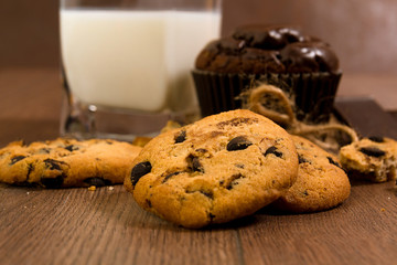 Cake and biscuits with chocolate chips and frosting. Glass of milk for breakfast on the wooden table.