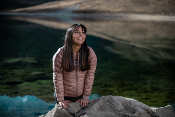 Naklejka premium Girl smiling on a rock, wearing a pink jacket, in winter beside the lake in the mountains, in the Snowy Toluca.