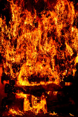 amazing violent bonfire of fire in a village in the dark night. The combustion of firewood creates big flames, flares, smoke, gas and generates a wide light around the fire. Vertical photo.