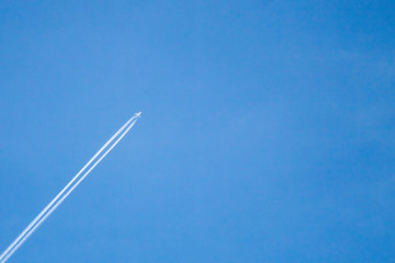A white passenger plane flies high in the sky leaving behind a Condensation, inversion and jet trail