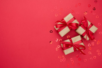 Gift boxes wrapped with kraft paper and red bow isolated on red background. Abstract flat lay.