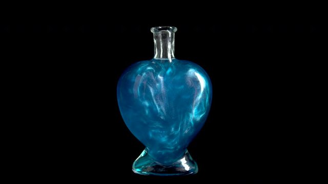 Glass bottle in the form of a heart with blue liquid. The elixir is spinning and overflowing with liquid. Potion of love is isolated on a black background.