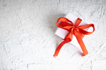 Gift box for Valentine's Day. View of present box package decorated into the white paper and red bow-knot. Flat lay on white background. ..