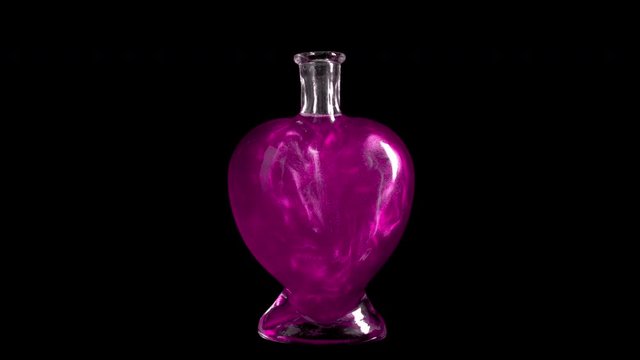 Glass bottle in the form of a heart with pink liquid. The elixir is spinning and overflowing with liquid. Potion of love is isolated on a black background.