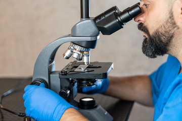 Male laboratory assistant examining biomaterial samples in a microscope