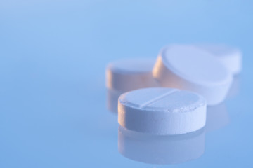 White round pills on a blue mirror surface with copy space, close up. Medicines on glass lit by the morning sun.