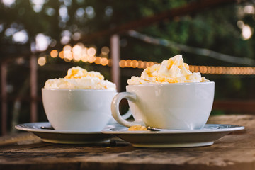 Two cups of coffee with chantilly on wooden table with outdoor lights background