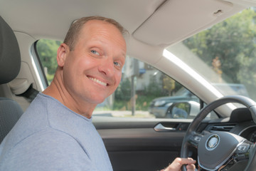 Portrait of happy owner of new automobile. Blond man took out an insurance policy for his new car, feel joy and smiling. Soft color image, horizontal and close-up.
