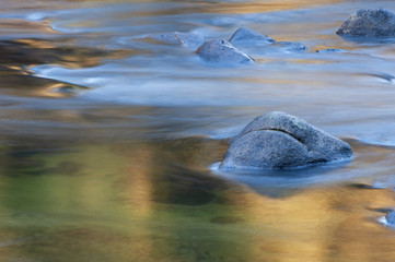 Merced River illuminated with reflected golden color from sunlit cliffs at sunrise and captured with motion blur, Yosemite National Park, California, USA