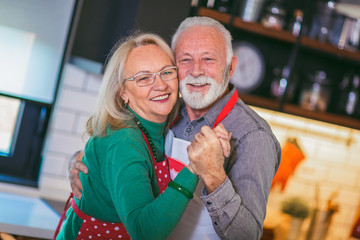 Beautiful senior couple is dancing and smiling while cooking together in kitchen