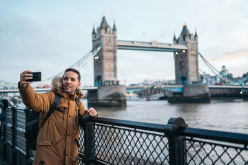 Young Man taking a photo with the smart phone to the Tower Bridge in London on a sunny winter day, London, Great Britain.