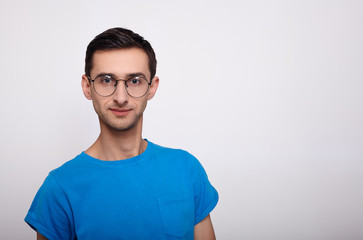 Portrait of a serious young man with glasses and a blue T-shirt on a white background.