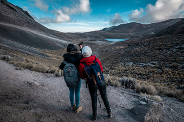 Fototapeta premium Girl scouts looking at the landscape and discovering new lands between the mountains, wearing winter clothes, where there is snow and the clouds touch the mountain tops, and take a selfie