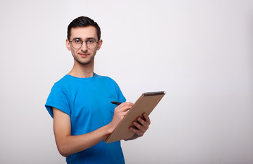 A young man with a notebook in his hands looks into the camera against a white background.