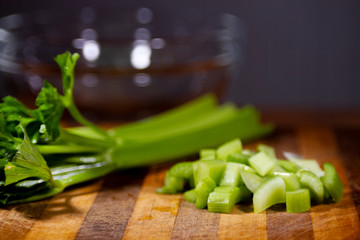 Celery, chopped an whole on a wooden cutting board with glass bowl in background