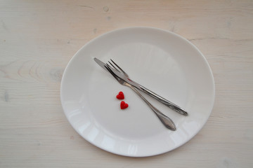 Festive table setting for Valentine's Day with fork, knife and heart on a white wooden table. Top view.