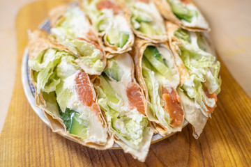Tortilla rolls with salmon, tender cheese, lettuce and fresh cucumber close-up on a plate