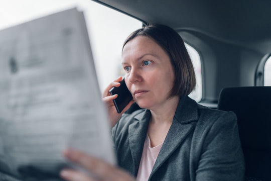 Businesswoman reading newspaper and using mobile phone at car backseat