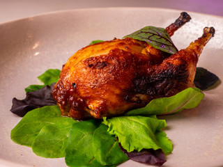 Baked cooked quail bird in a plate close-up in green leaves