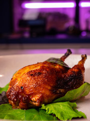 Baked cooked quail bird in a plate close-up in green leaves