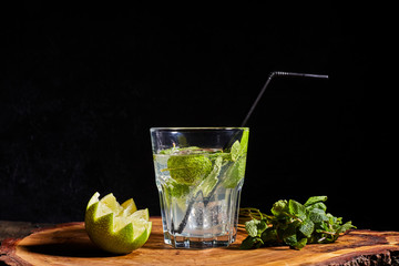 Fresh drink with lime, mint and ice on wooden table on dark background