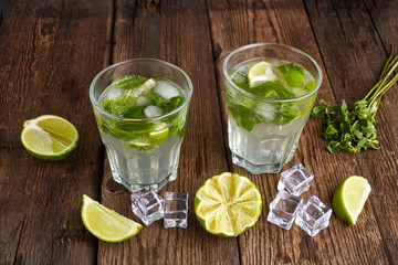 Fresh mojito in glasses with ice cubes on wooden table.