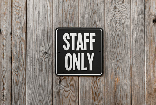 Black and white square STAFF ONLY sign attached to a wooden wall.