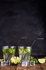 Fototapeta premium Fresh drink with lime, mint and ice on wooden table on dark background. Portrait, vertical format. Copy space.