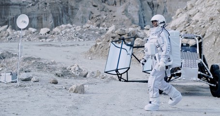 Female astronaut walking on the Moon ground in the valley while arriving to do investigations. Outdoors. Explorations in the space.