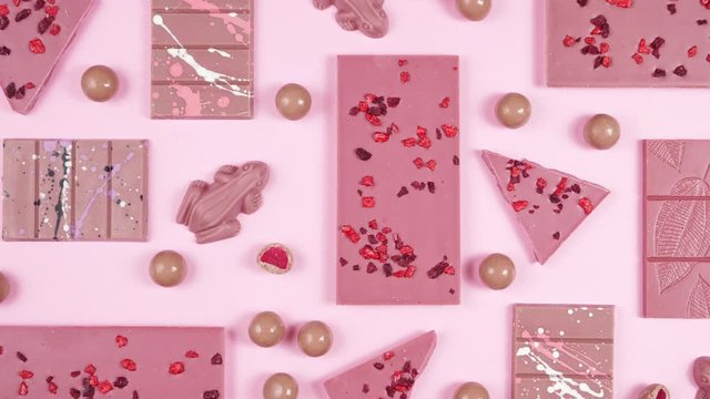 Ruby chocolate selection, made from botanical cocoa bean varieties that have the right attributes to be processed into ruby chocolate, panning flat lay on pink background.