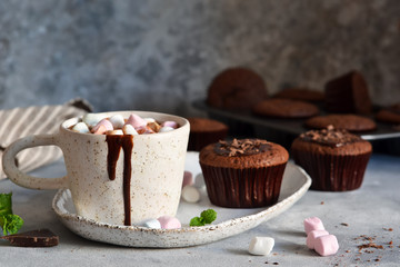 Christmas drink - hot chocolate with marshmallows and a cupcake on a concrete background.