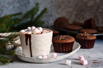 Christmas drink - hot chocolate with marshmallows and a cupcake on a concrete background.