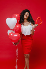 playful black woman with heart shape and colorful balloons on red background