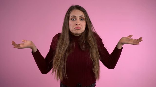Misunderstanding and perplexity gestures, displeased woman throwing her hands wide and showing her real emotions. Woman shaking shoulders in despair, portrait of perplexed woman over studio pink