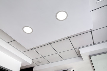 multi-level ceiling with three-dimensional protrusions and a suspended tiled ceiling with a built-in round led light, white color. - obrazy, fototapety, plakaty