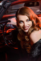 Fototapeta na wymiar Retro portrait of a beautiful luxury Gatsby woman in black cabriolet car. Vogue fashion style and smoke. Model with a hollywood smile. Copy space