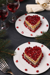 Festive salad in layers in the shape of a heart, decorated with pomegranate seeds on a dark background, Vertical orientation
