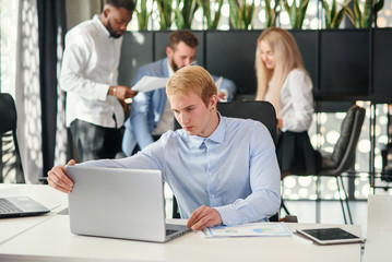 Enterprising caucasian office manager sitting at his workplace at office and studying report's datas in the meeting room.