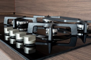 A detail of a modern gas cooker with ceramic hob and a dark brown wooden kitchen ready for cooking a meal