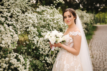 Charming bride in gorgeous wedding dress hold bouquet and stand in front of blooming trees